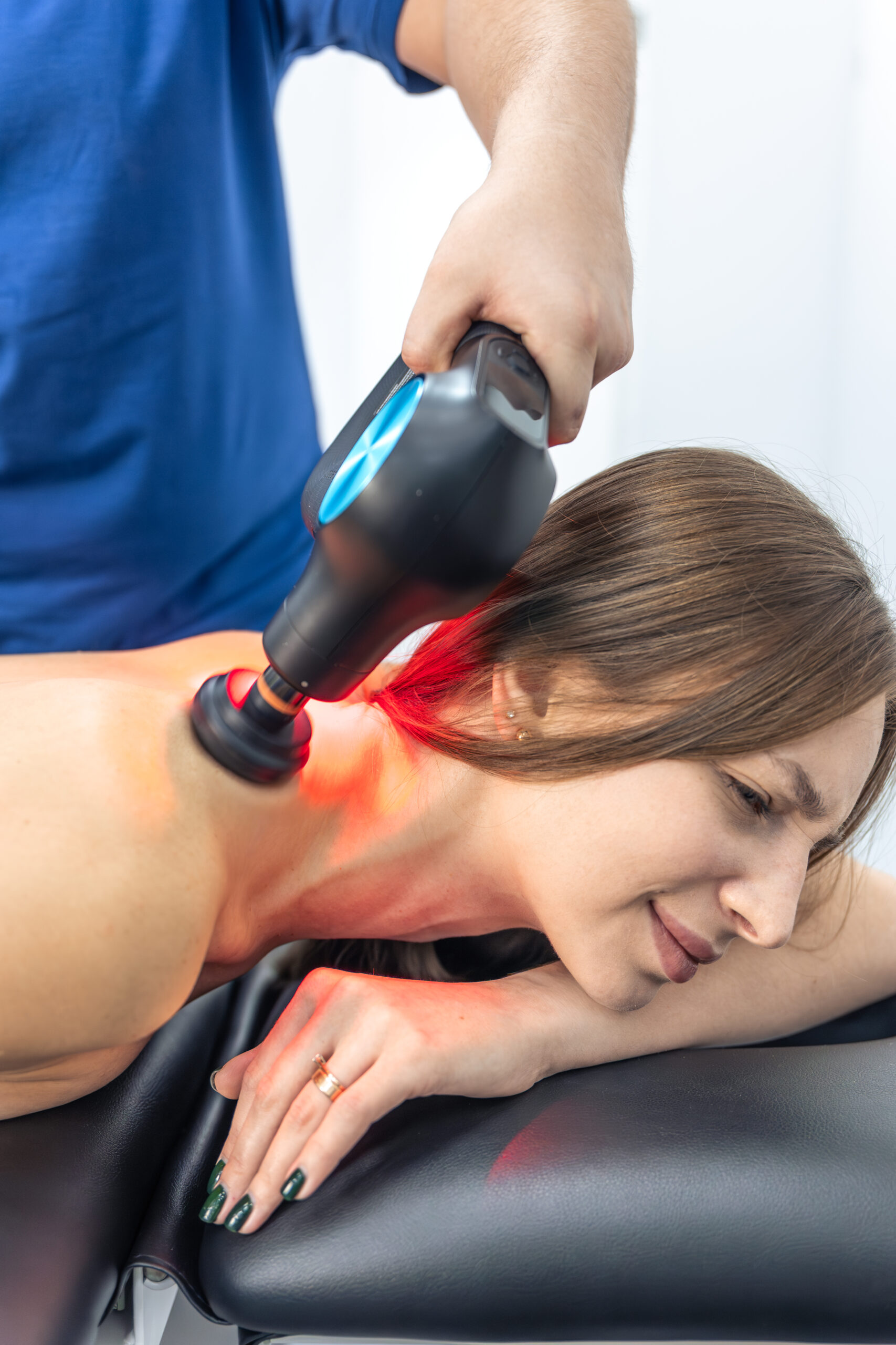 Therapist using laser therapy device on female patient's shoulder and collarbone area for pain management and rehabilitation support.